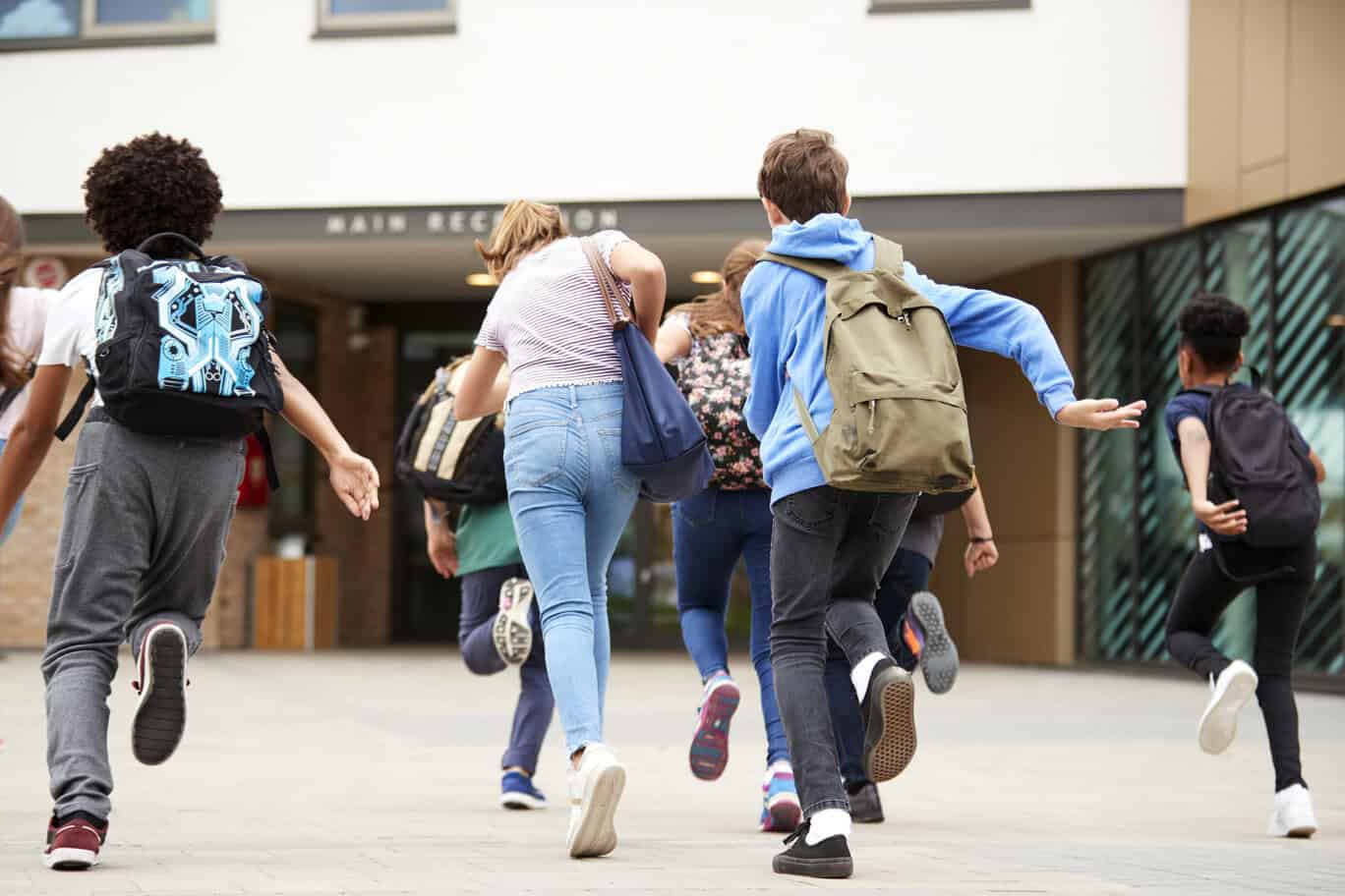 group of high school students running into school building at beginning of class